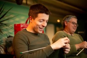 Two members of Dutch Language café knitting a scarf while smiling and looking at their knitting.